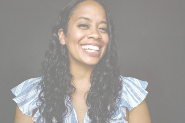 Photo of Paige, a woman with long curly black hair, wearing a white and blue blouse, smiling to camera